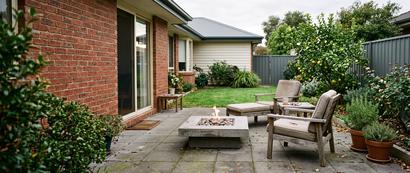 A concrete fire table alight on a tidy suburban Australian patio beside outdoor lounge chairs