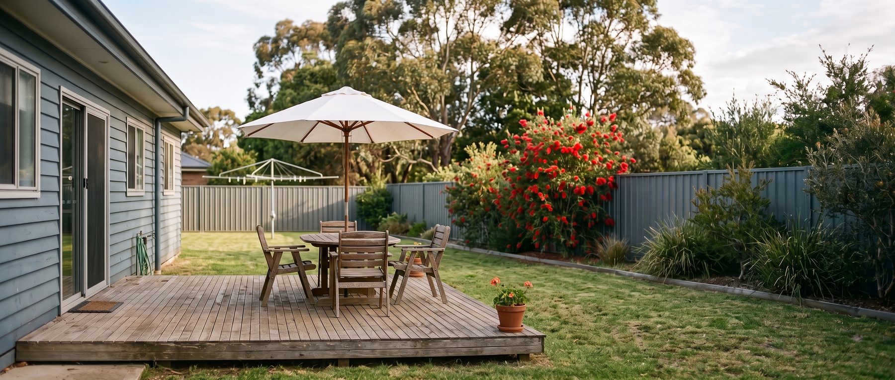 Market umbrella over an outdoor dining table on a timber deck in a suburban backyard