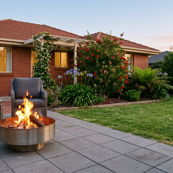 Solid stainless steel fire bowl with an open flame on a suburban patio at dusk