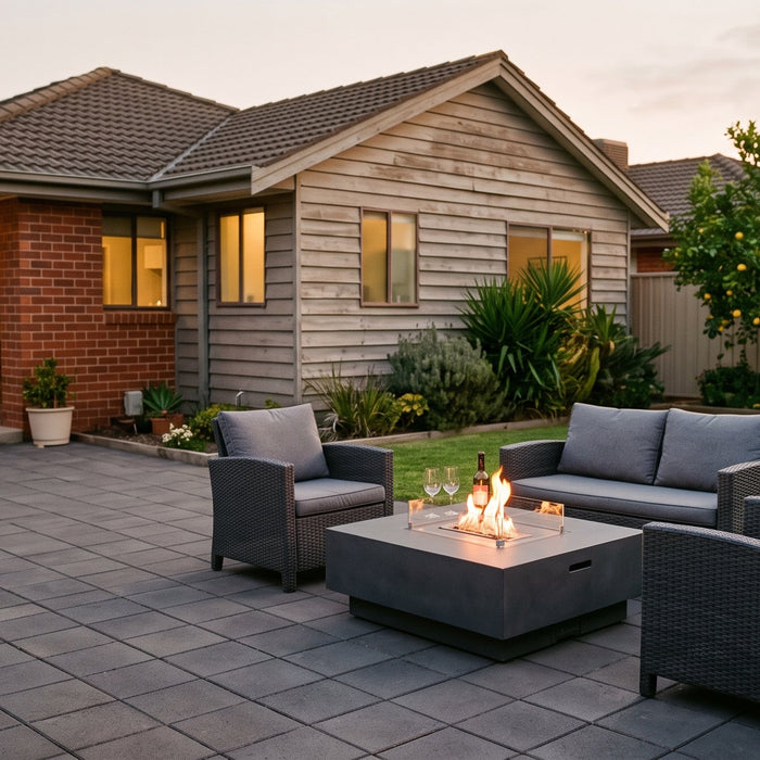 A concrete bioethanol fire table with lounge seating on a paved patio in a normal Australian suburban backyard at dusk