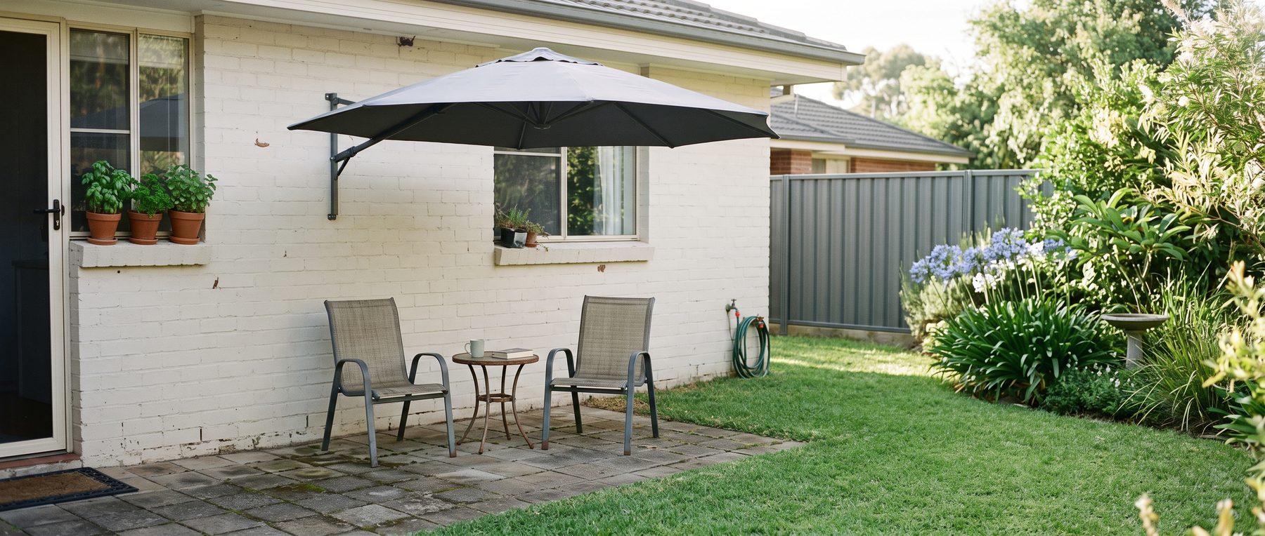 Wall-mounted umbrella on a bracket shading two chairs on a small suburban patio
