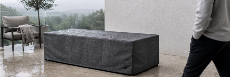 Premium charcoal fire table cover with rain droplets on a modern outdoor patio during an overcast morning.