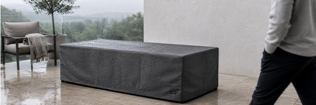 Premium charcoal fire table cover with rain droplets on a modern outdoor patio during an overcast morning.