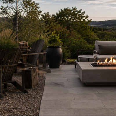 Rustic wood fire pit beside a modern gas fire table on a split Australian backyard entertaining space at dusk.