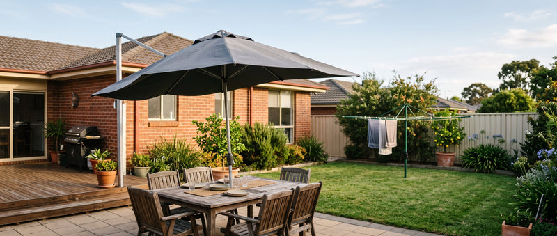 Cantilever patio umbrella catching a breeze over a timber deck dining setting in a tidy Australian suburban backyard