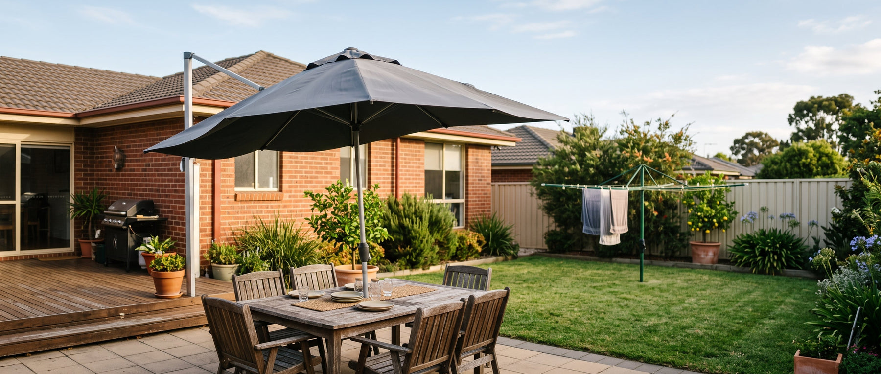 Cantilever patio umbrella catching a breeze over a timber deck dining setting in a tidy Australian suburban backyard