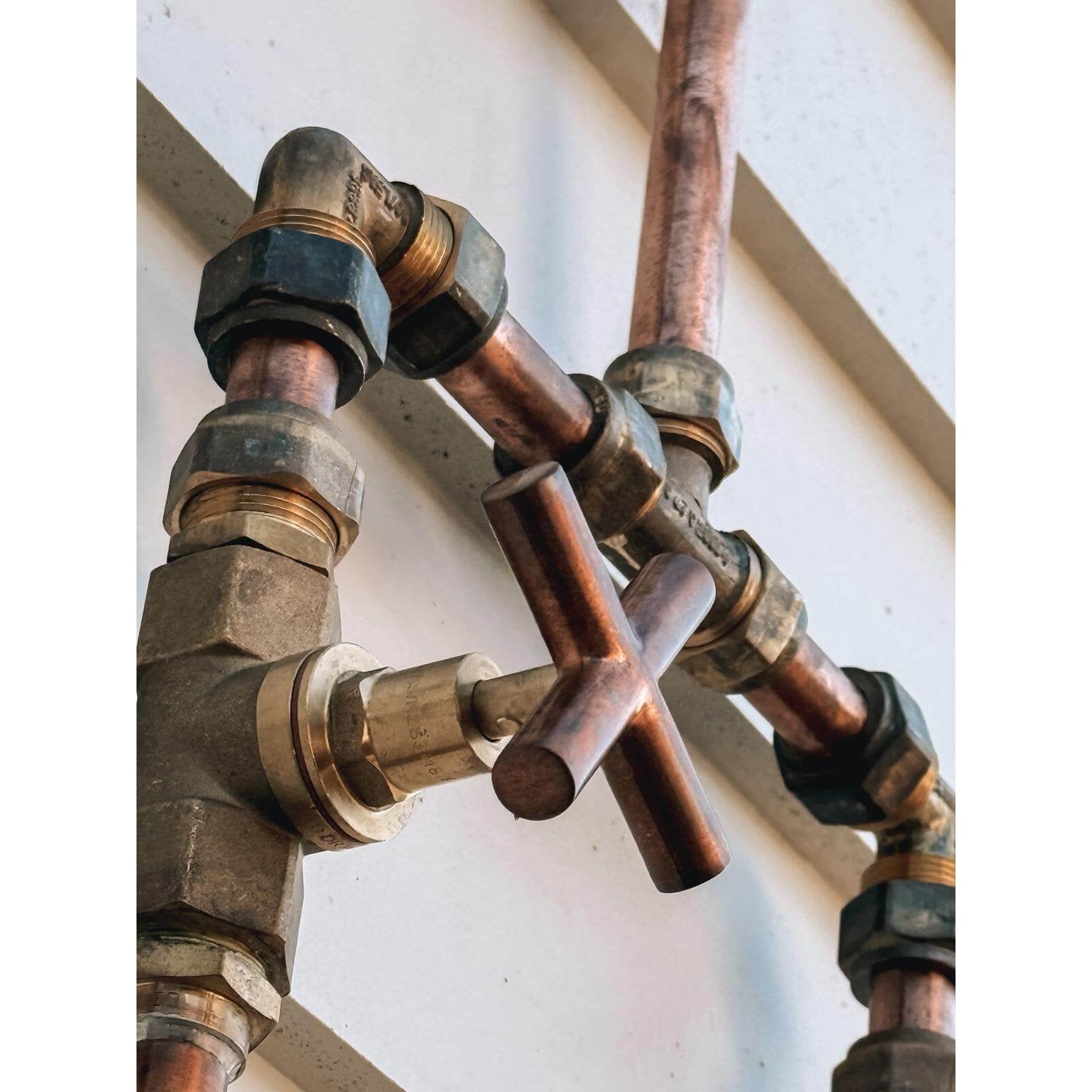 Handmade Banksia copper and brass hot and cold outdoor shower mounted against a wall.