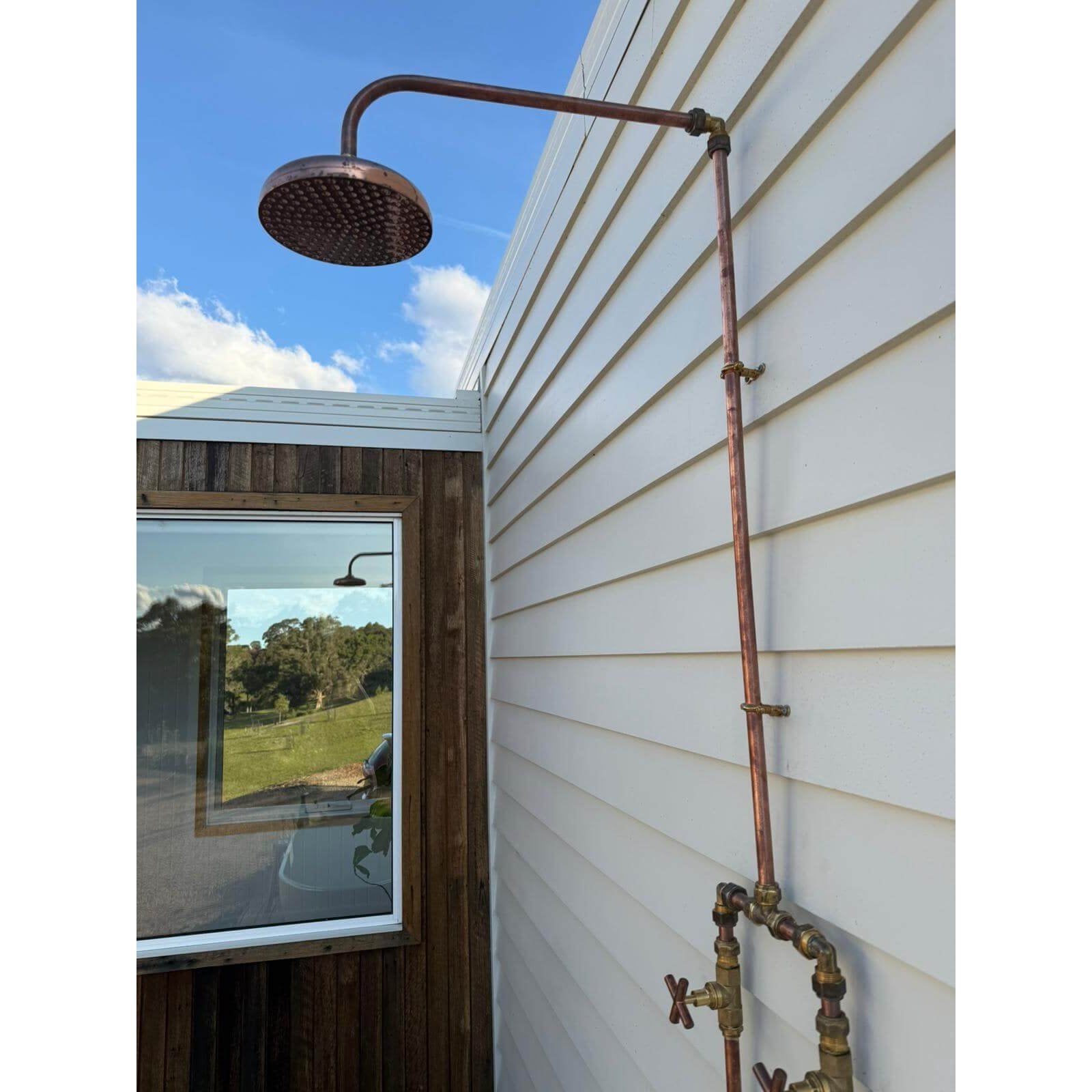 Handmade Banksia copper and brass hot and cold outdoor shower mounted against a wall.