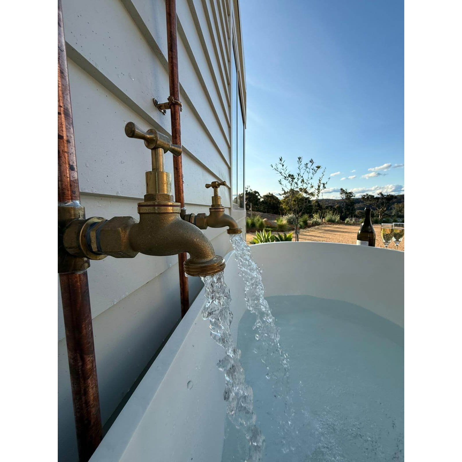 Handmade Banksia copper and brass hot and cold outdoor shower mounted against a wall.