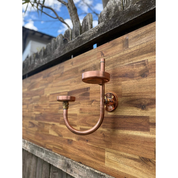 Handmade copper and brass soap, drink and plant holder beside an outdoor copper shower.