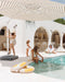 Solstice cantilever umbrella, White frame, Taupe Stripe canopy, poolside resort setting with family