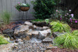 A backyard waterfall fountain built with the Aquascape Landscape Fountain Kit, water disappearing into a pebble bed surrounded by planting