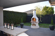 Buschbeck Rondo Outdoor Fireplace lit at dusk beside an outdoor dining table with lanterns