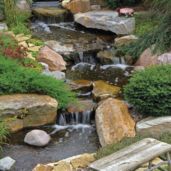 An 8m pondless waterfall stream built with the Aquascape Large Pondless Waterfall Kit, running through a landscaped garden past a timber bench