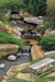An 8m pondless waterfall stream built with the Aquascape Large Pondless Waterfall Kit, running through a landscaped garden past a timber bench