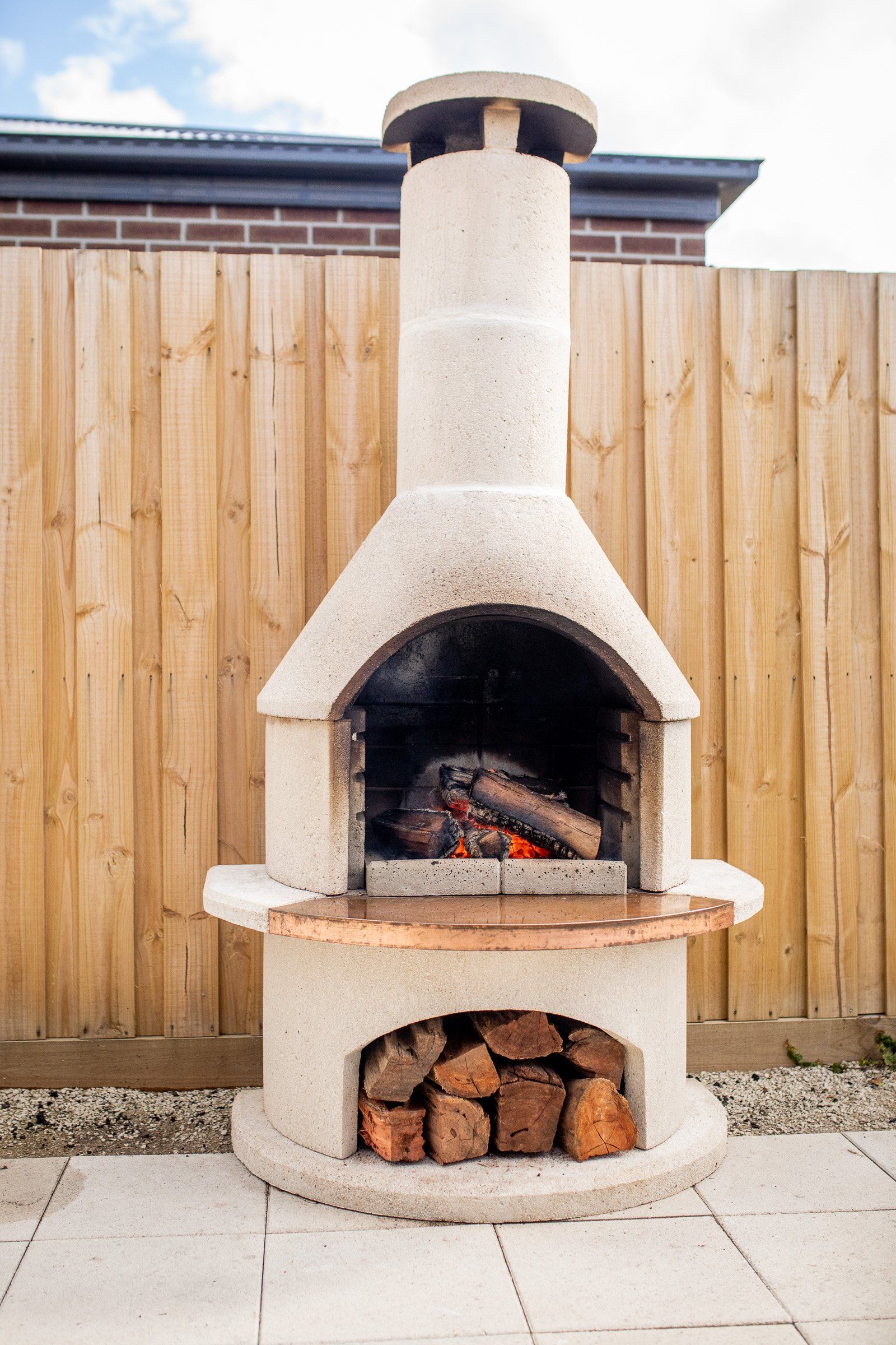 Buschbeck Rondo Outdoor Fireplace lit during the day on a paved patio