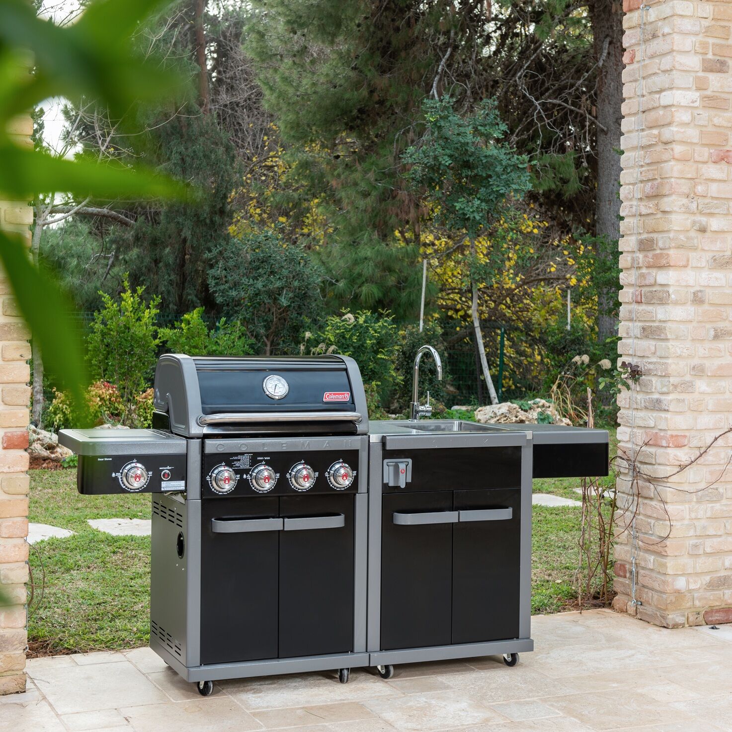 Coleman Revolution 4 Burner outdoor kitchen with the sink module in a garden setting