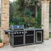 Coleman Revolution 4 Burner outdoor kitchen with sink and fridge modules beside a brick pillar