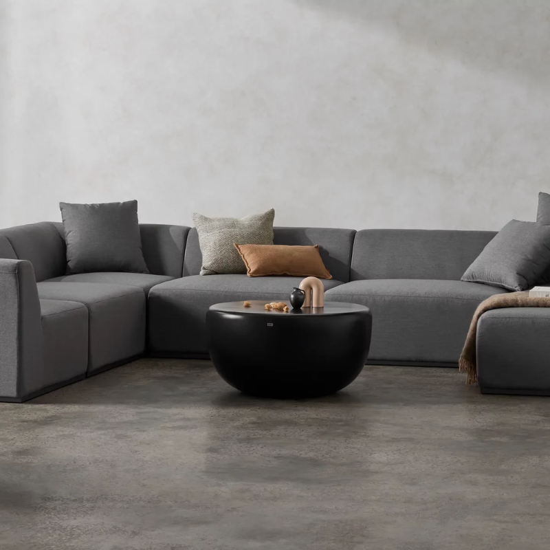 Node 30 round concrete coffee table in graphite finish styled in a modern living room with sectional sofa