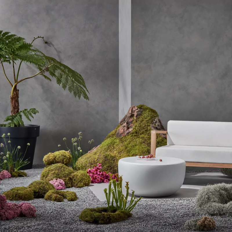 White Node 30 round concrete coffee table styled outdoors with modern seating and greenery