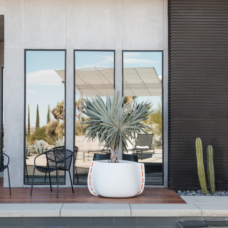 Blinde Stitch 50 white concrete planter with orange stitched rope detail placed outside a modern home with large glass windows