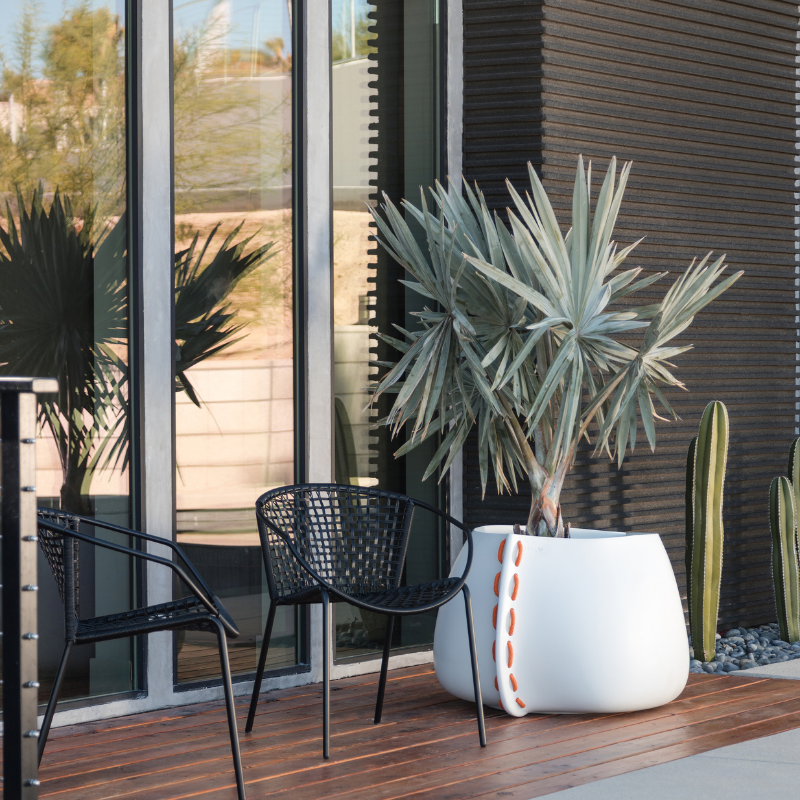 Blinde Stitch 50 white concrete planter with orange stitched rope detailing on a modern patio beside black outdoor chairs