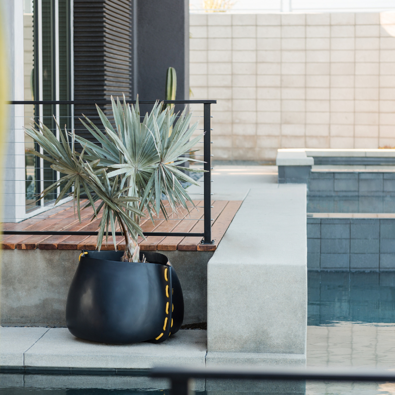Blinde Stitch 75 concrete planter with yellow stitched detail placed poolside on a modern outdoor patio with a palm plant