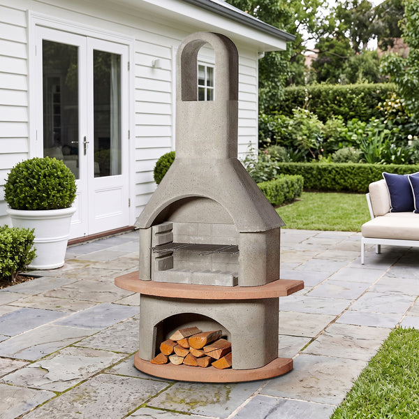 Buschbeck Carmen 3-in-1 outdoor fireplace, BBQ and pizza oven with hooped flue and terracotta shelf, on a bluestone terrace beside a white weatherboard home