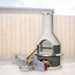 Buschbeck Rondo 3-in-1 outdoor fireplace, BBQ and pizza oven kit in Grey with the pizza oven door, peels, cutter and base extension, shown in a backyard setting