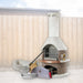 Buschbeck Rondo 3-in-1 outdoor fireplace, BBQ and pizza oven kit in Mocha with the pizza oven door, peels, cutter and base extension, shown in a backyard setting