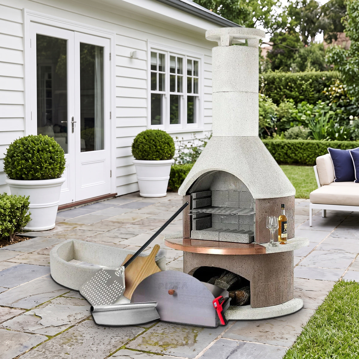 Buschbeck Rondo 3-in-1 outdoor fireplace, BBQ and pizza oven kit in Mocha with pizza oven door, base extension, peels and cutter, on a bluestone terrace beside a white weatherboard home