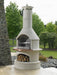 Buschbeck Rondo 3-in-1 outdoor fireplace, BBQ and pizza oven in White, with copper shelf and wood store, in a garden beside a stacked stone wall