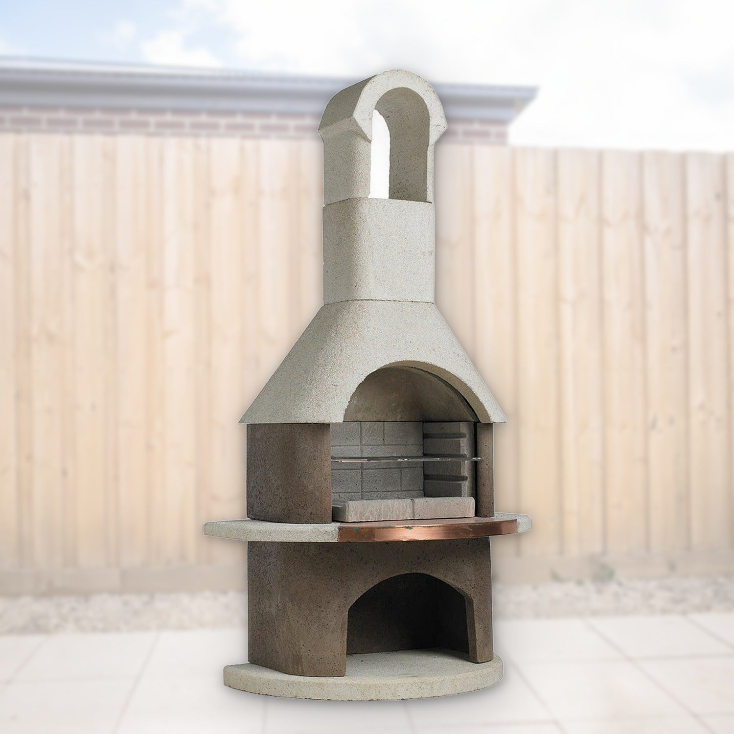 Buschbeck St Moritz 3-in-1 outdoor fireplace, BBQ and pizza oven with copper shelf and wood store, shown in a backyard setting