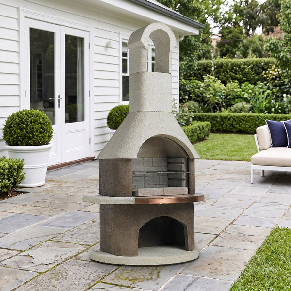 Buschbeck St Moritz 3-in-1 outdoor fireplace, BBQ and pizza oven with arched flue and copper shelf, on a bluestone terrace beside a white weatherboard home