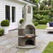 Buschbeck St Moritz 3-in-1 outdoor fireplace, BBQ and pizza oven with arched flue and copper shelf, on a bluestone terrace beside a white weatherboard home