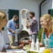 Friends entertaining around the Buschbeck St Moritz Outdoor Fireplace on a sunny patio