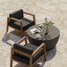 Dark metal Circ 40 round coffee table styled outdoors with lounge chairs and coffee cups