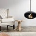 Cocoon Aeris Hanging Bioethanol Fireplace in matt black hanging beside a wingback armchair