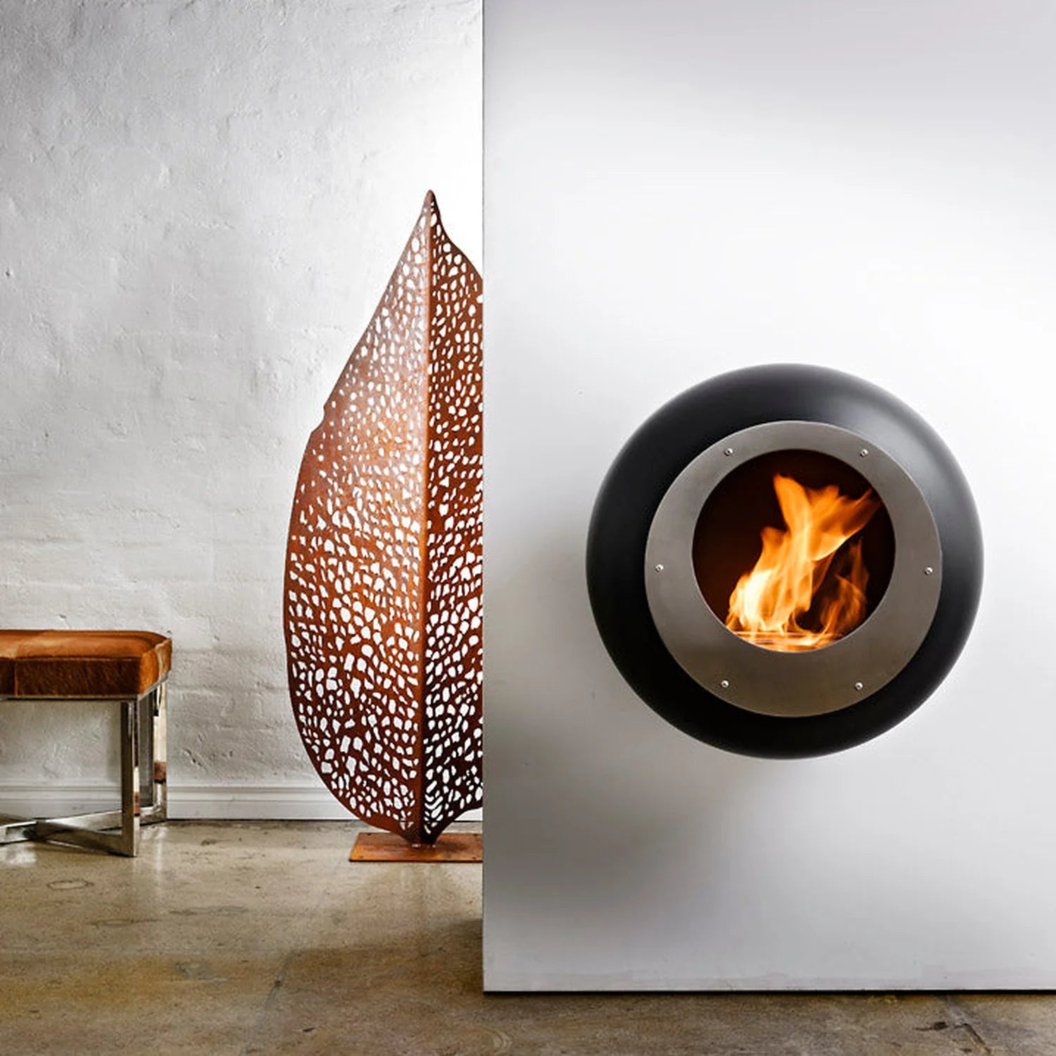 Cocoon Vellum Wall Mounted Bioethanol Fireplace in black on a white wall beside a leaf sculpture