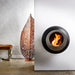 Cocoon Vellum Wall Mounted Bioethanol Fireplace in black on a white wall beside a leaf sculpture