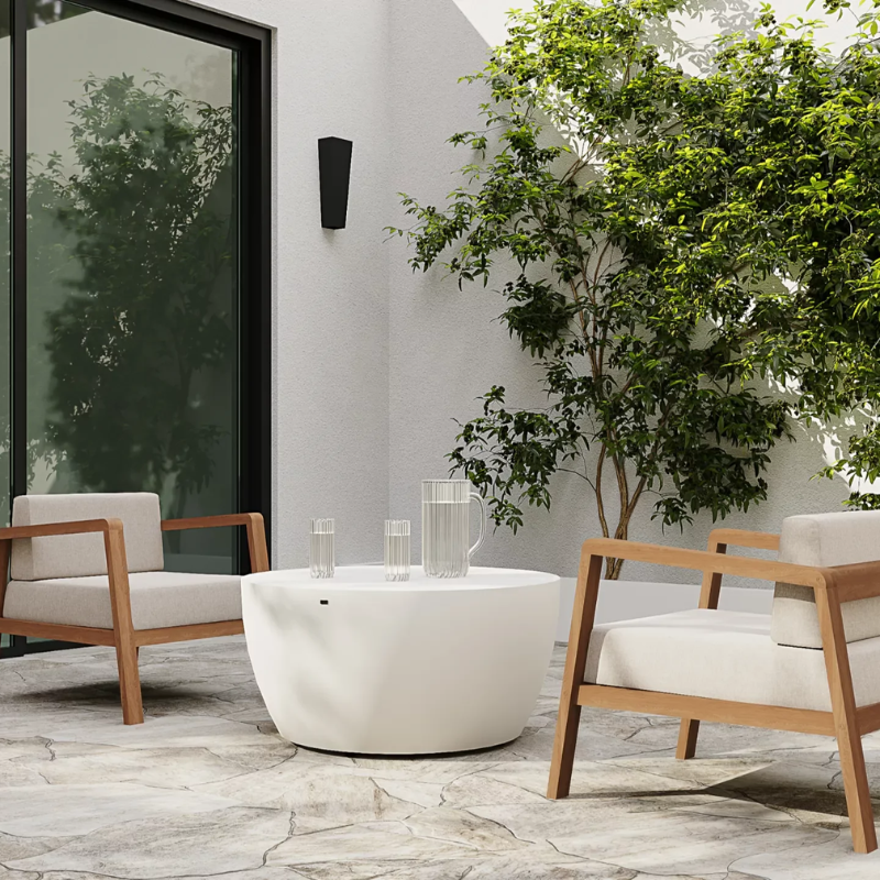 White Curv 30 round coffee table styled on a modern outdoor patio with wooden lounge chairs and greenery