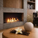 Vanilla pods and orchid on a coffee table beside a lit linear bioethanol fireplace