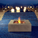 EcoSmart Base 40 fire table placed by poolside at night with glowing lights and water reflections