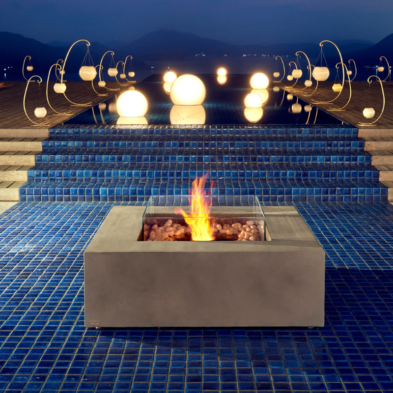 EcoSmart Base 40 fire table placed by poolside at night with glowing lights and water reflections