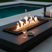 EcoSmart Linear 50 Fire Pit Kit set with stainless steel burner in a luxurious poolside outdoor area, with flames dancing over black glass rocks, surrounded by drinks and olives, creating a sophisticated atmosphere for evening gatherings