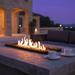 EcoSmart Linear 50 Fire Pit Kit with black burner in a luxurious outdoor setting at dusk, featuring flames over black glass rocks, accompanied by two cups for a relaxing gathering.