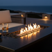 EcoSmart Linear 65 Fire Pit Kit featuring a black burner in a modular design, placed on a stone table with a fire burning brightly