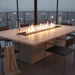 EcoSmart Linear 90 Fire Pit Kit integrated into a luxurious dining table, set against a city skyline, with a long flame burning through the center.