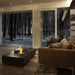 EcoSmart Martini 50 fire table in a living room with a glass screen and a forest outlook.
