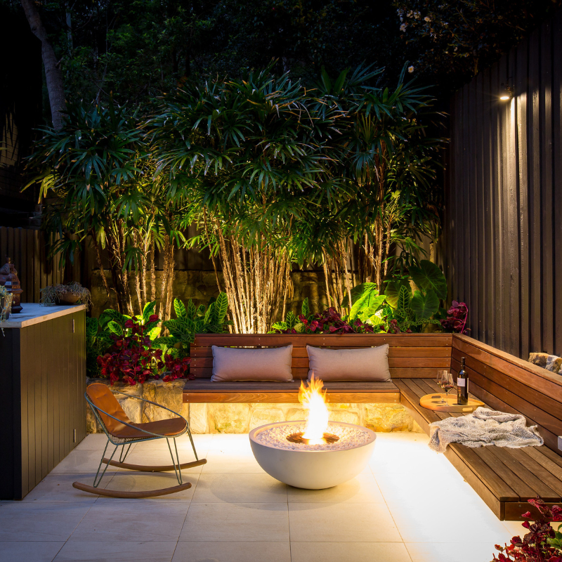 EcoSmart Mix 850 Fire Pit in Bone finish at night on a modern patio with rocking chair and warm flame.